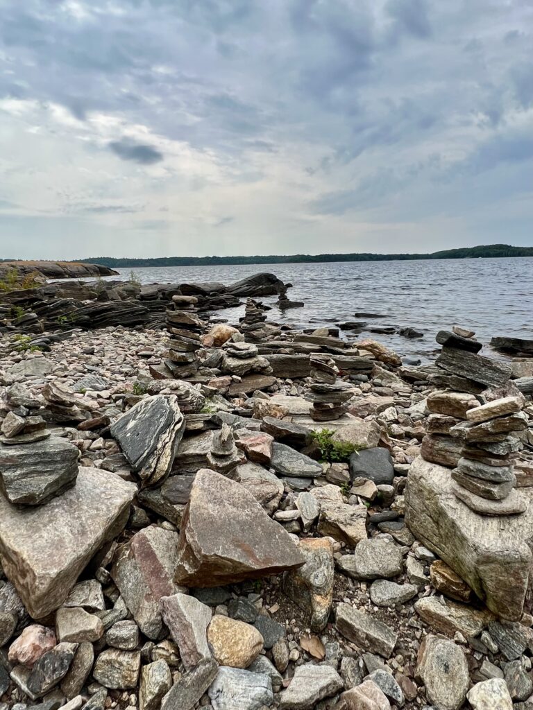 A scenic view of Lake Huron in Parry Sound, Ontario, features rocky shores with stacked stone formations under a cloudy sky. A natural representation of Canada’s rugged beauty, symbolizing strength, resilience, and local craftsmanship — core values of TheCanadianSellers.ca.